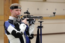 Man in shooting uniform standing with air rifle.