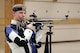 Man in shooting uniform standing with air rifle.