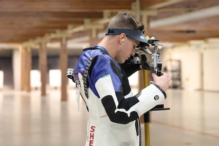 Man in shooting uniform standing with air rifle.