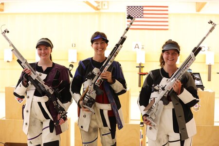 Three women in shooting uniforms standing with air rifles.