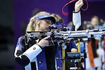 Woman in shooting uniform standing with air rifle.