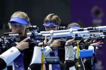 Three women in shooting uniforms standing with air rifles.