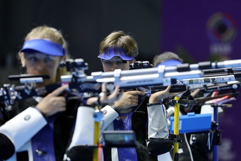 Three women in shooting uniforms standing with air rifles.