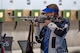 Man in shooting uniform standing with air rifle.