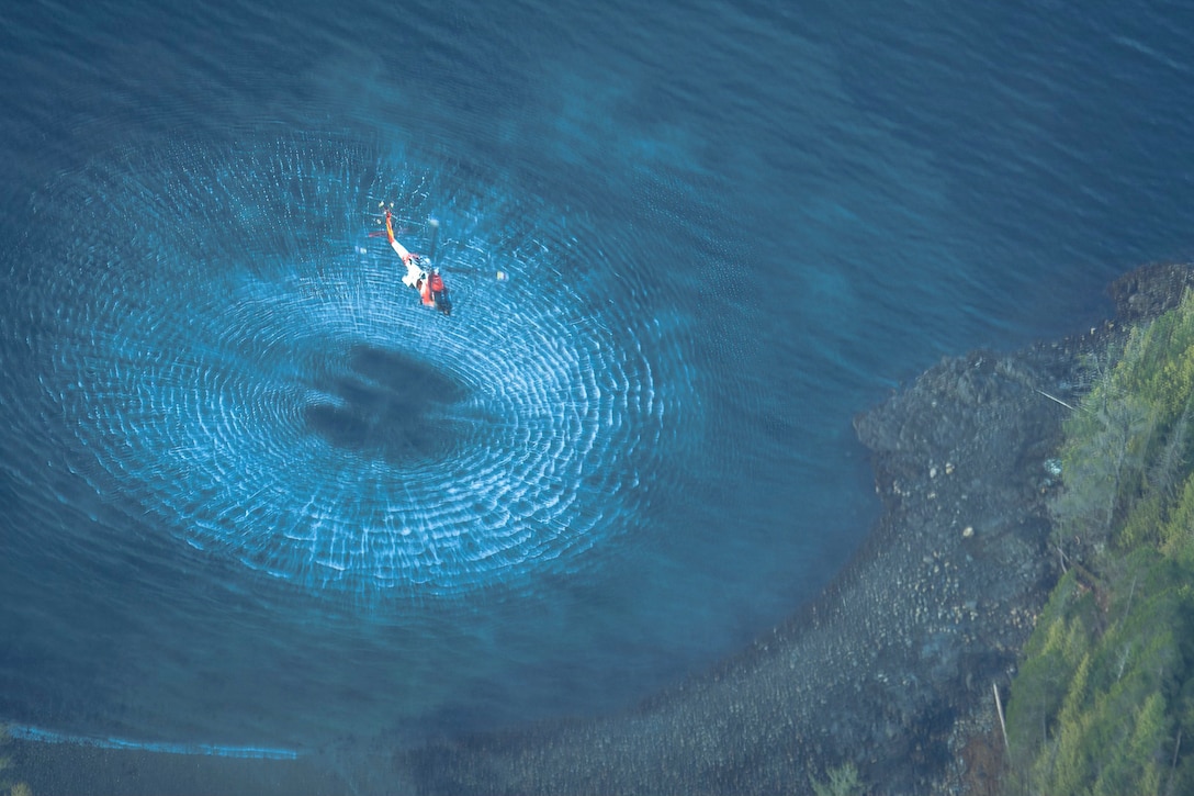 A helicopter hovers over a body of water as seen from above.