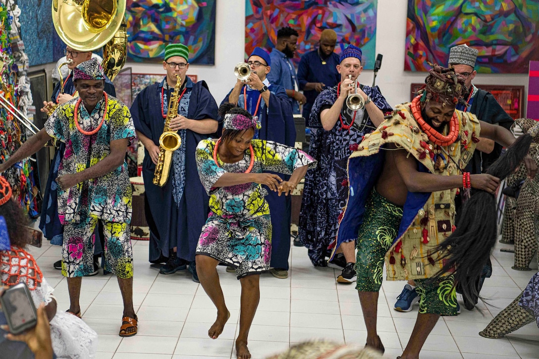 Nigerian artists and Navy band members dressed in Nigerian garb perform in front of an audience.