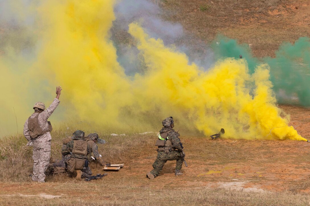 Marines kneel in a field surrounded by clouds of yellow and green smoke.