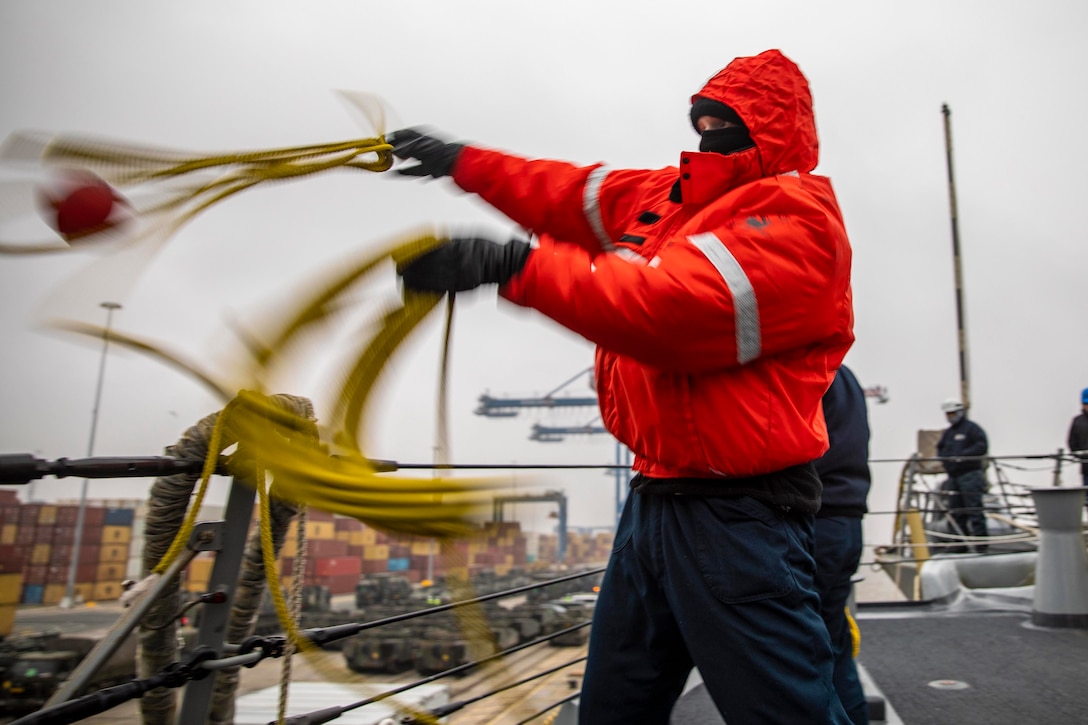 A sailor throws a rope over the rails of a ship.