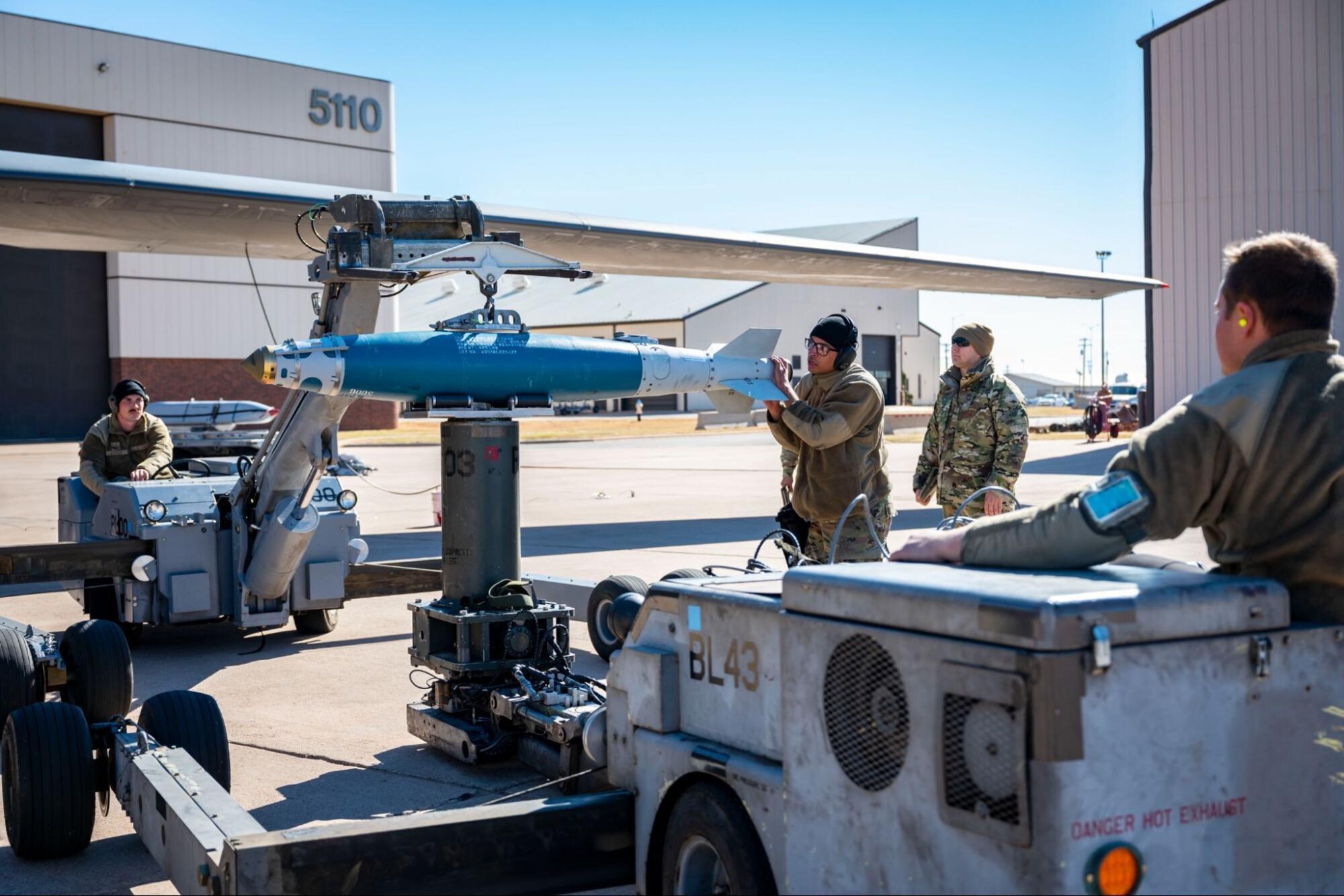 Weapons load crew members assigned to the 28th Aircraft Maintenance Unit, attach an inert bomb to a jammer during the Load Crew of the Year competition at Dyess Air Force Base, Texas, Jan. 27, 2023. Munitions Systems Airmen are enlisted Airmen that are tasked with protecting, handling, storing, transporting, arming/disarming, and assembly of non-nuclear munitions. (U.S. Air Force photo by Senior Airman Leon Redfern)