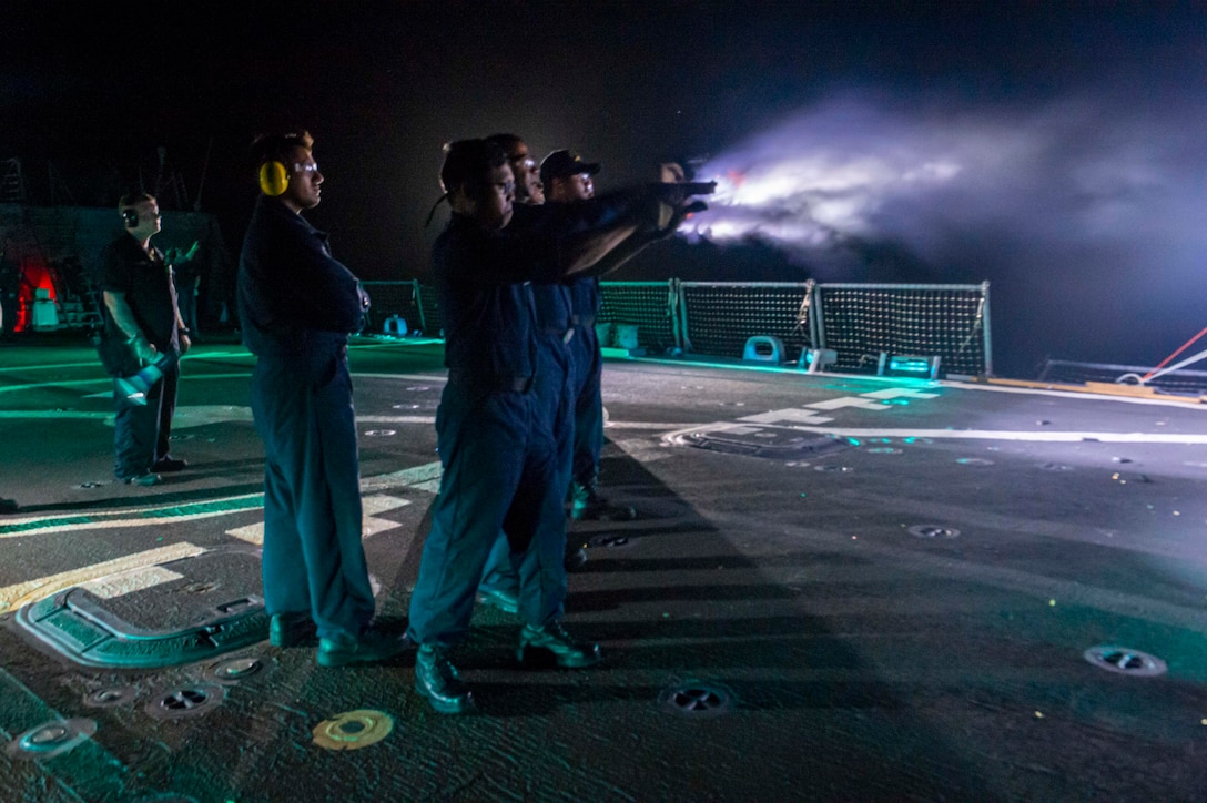 Soldiers fire weapons at night during training on the flight deck of a Navy ship.