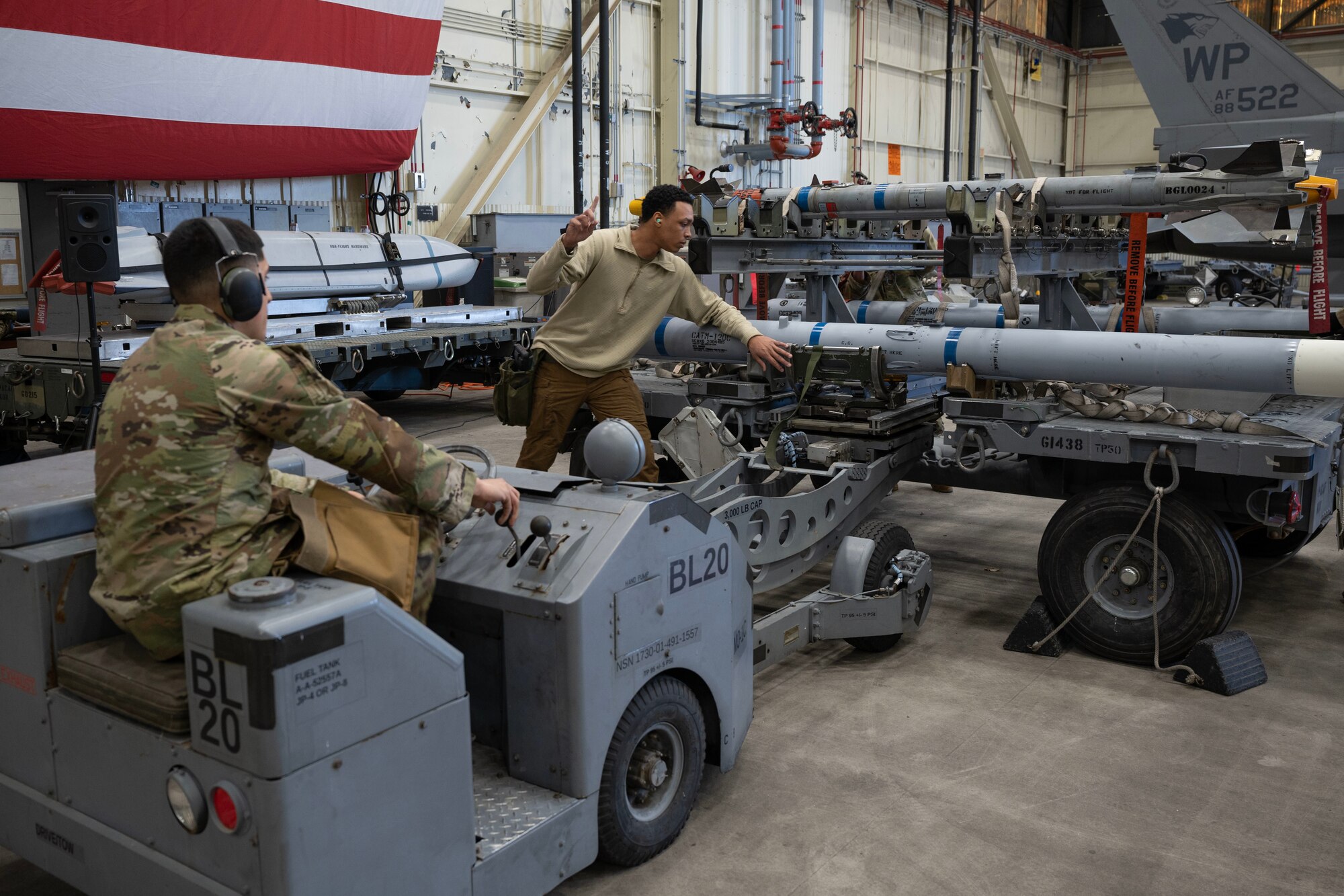 An Airman guides another Airman on picking up an Air Intercept Missile with a jammer vehicle.