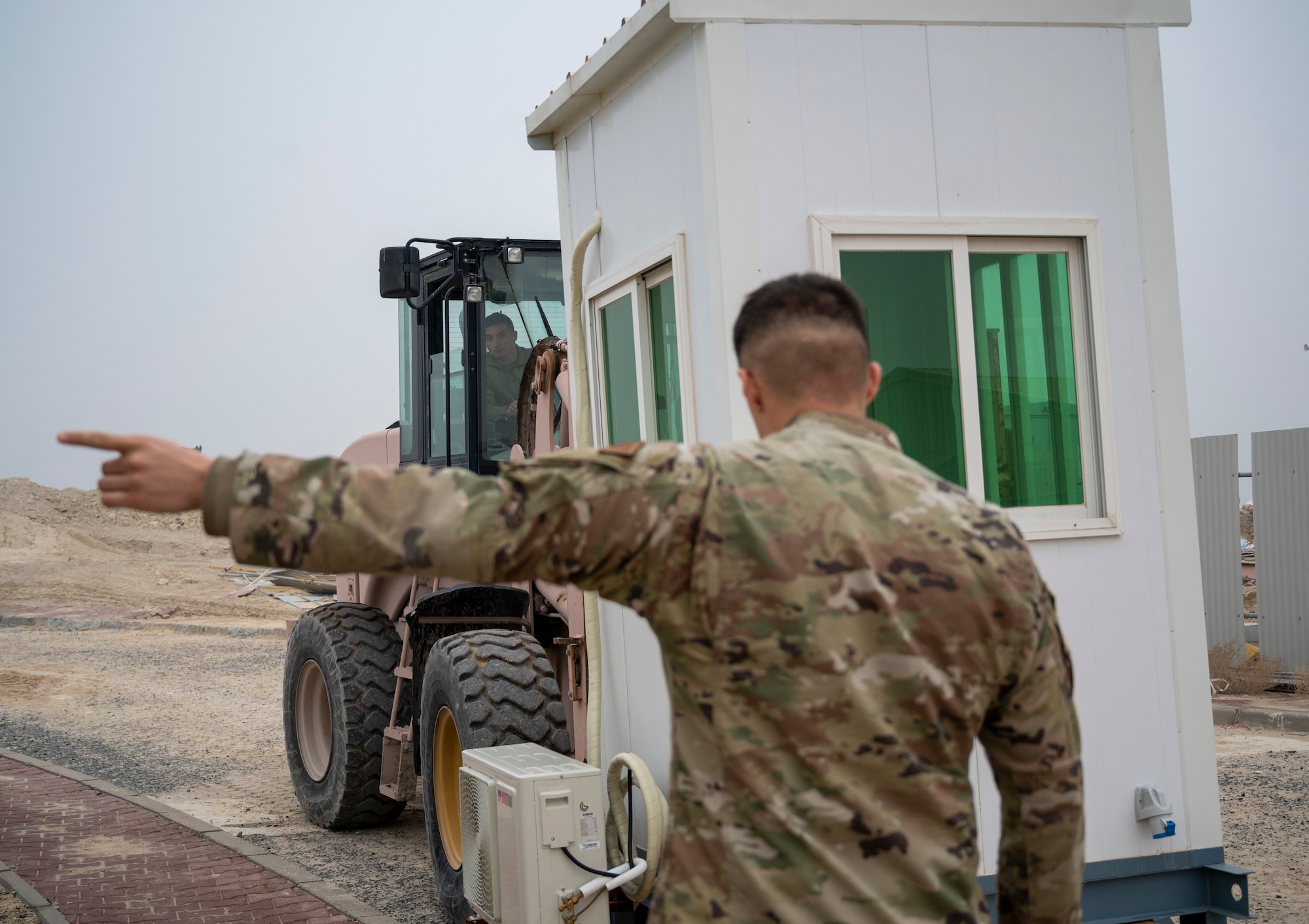 U.S. Air Force Airman 1st Class Isaiac Perez, 386th Expeditionary Civil Engineer Squadron pavements and heavy equipment apprentice, guides U.S. Air Force Airman 1st Class Felix Bojorquez, 386th ECES pavements and heavy equipment apprentice, as he places a new security cabin at Ali Al Salem Air Base, Kuwait, Jan. 25, 2023.