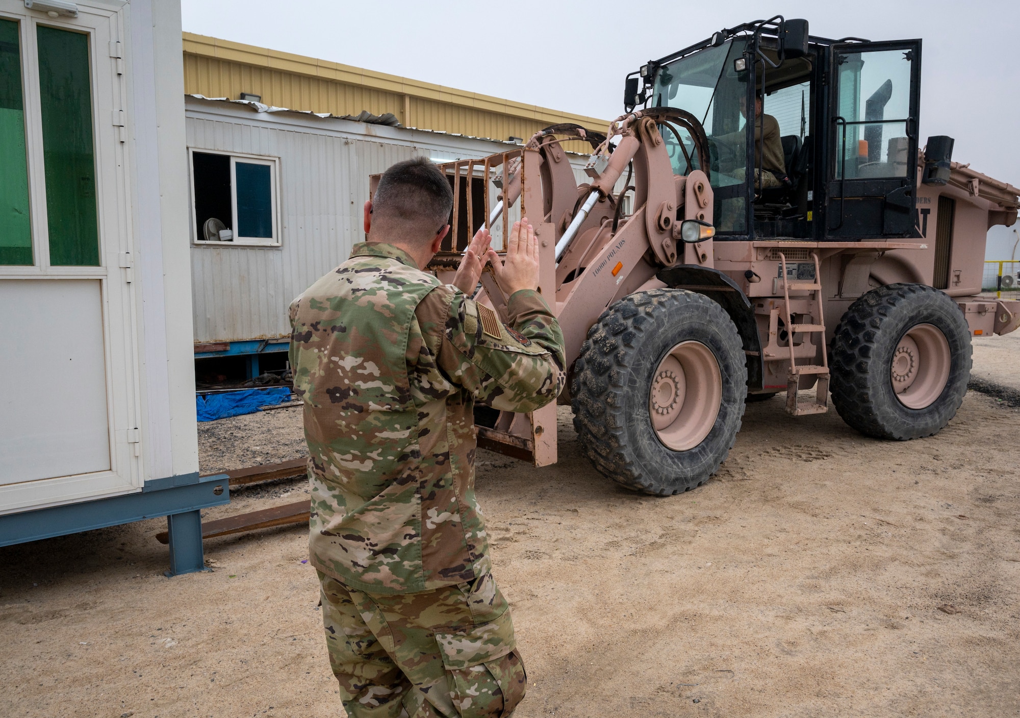 U.S. Air Force Airman 1st Class Isaiac Perez, 386th Expeditionary Civil Engineer Squadron pavements and heavy equipment apprentice, guides U.S. Air Force Airman 1st Class Felix Bojorquez, 386th ECES pavements and heavy equipment apprentice, as he places a new security cabin at Ali Al Salem Air Base, Kuwait, Jan. 25, 2023.