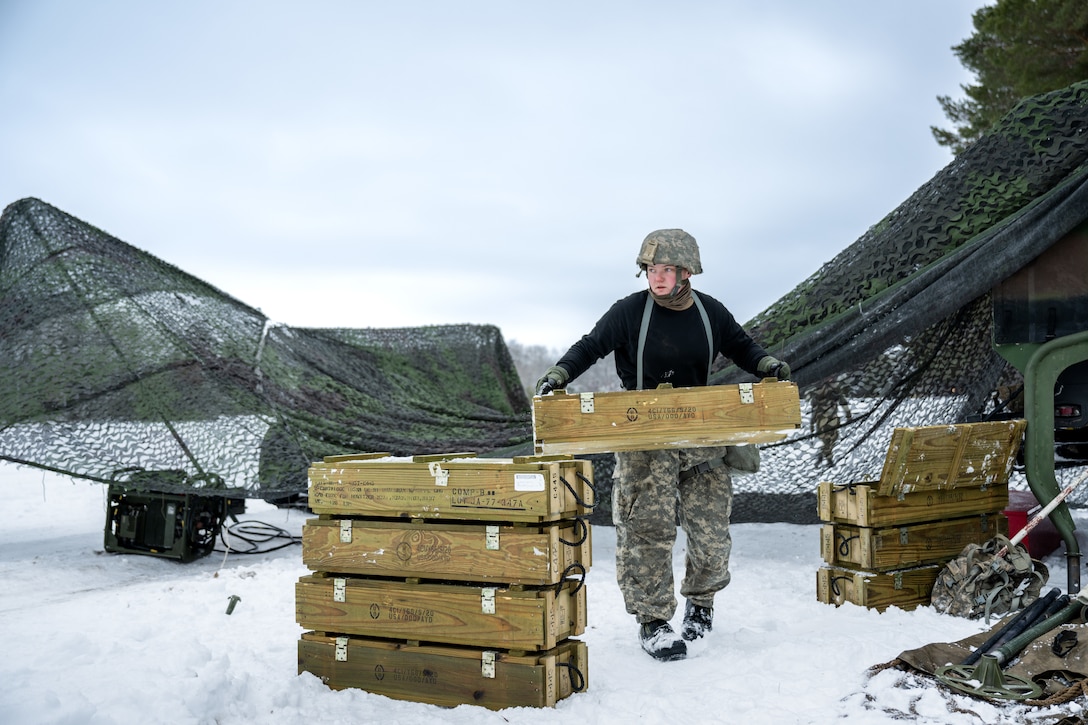 A soldier carries a wooden crate in the snow.