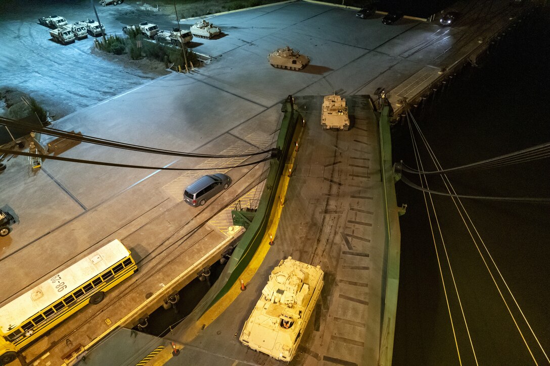 A convoy of Bradley tanks are loaded onto a vehicle carrier.