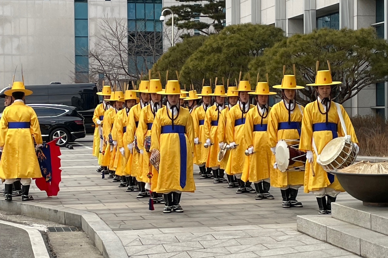 Band members dressed in traditional South Korean uniforms stand in rows.