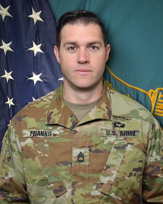 Man in U.S. Army uniform standing in front of two flags.