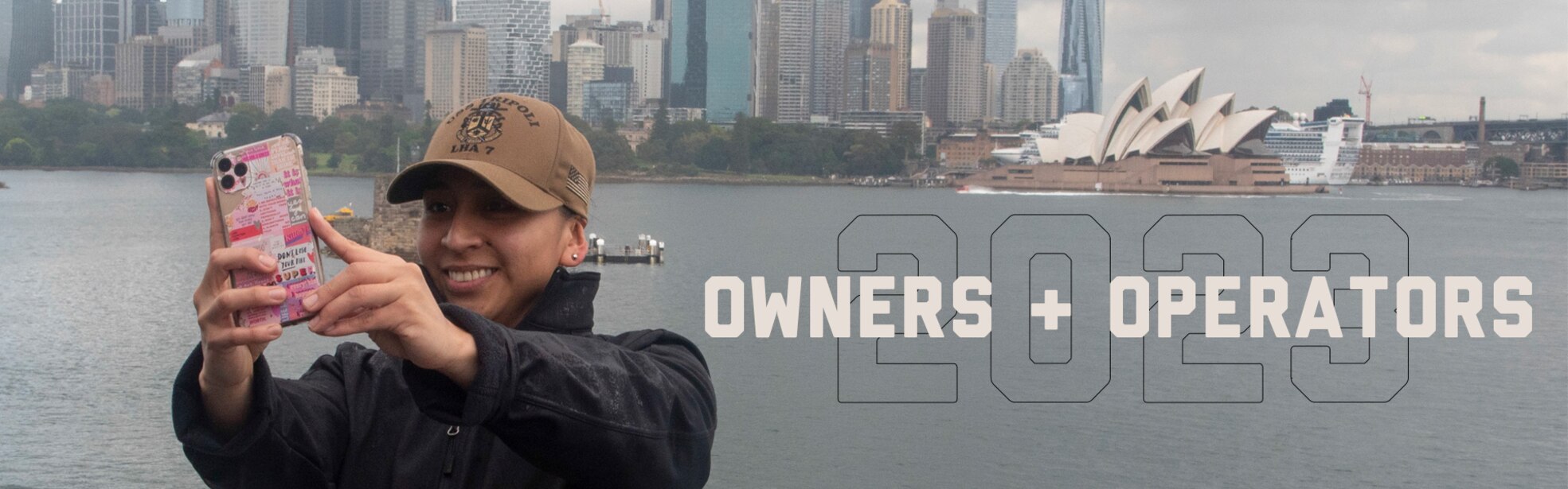 Sailor in jacket snapping a selfie with their phone with Sydney city skyline in background