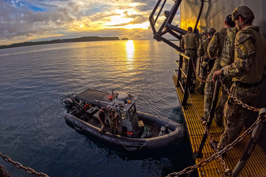 Sailors stand on a metal deck looking at a rubber power boat below them.
