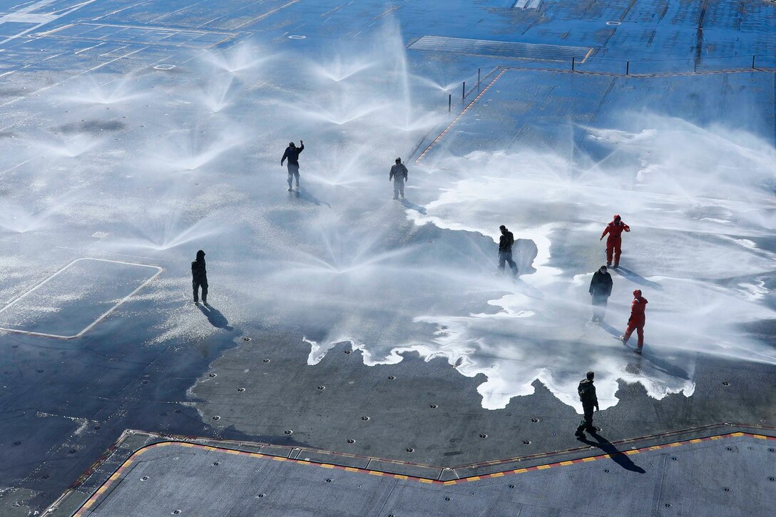Sailors walk through sprinklers on the deck of a ship.