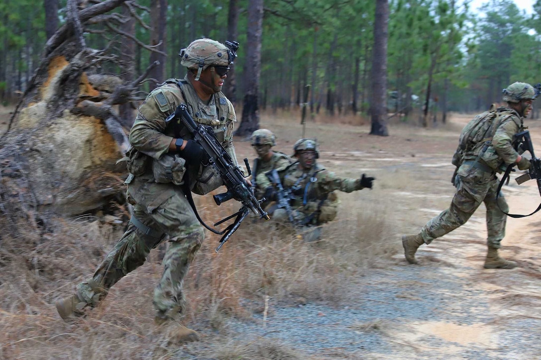 Soldiers run in a wooded area.