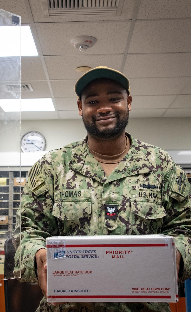 A man in uniform poses for a photo while holding a package.