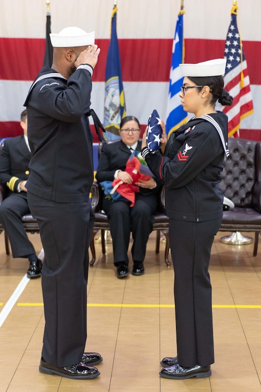 A man in military uniform renders a salute to a woman holding the American flag.