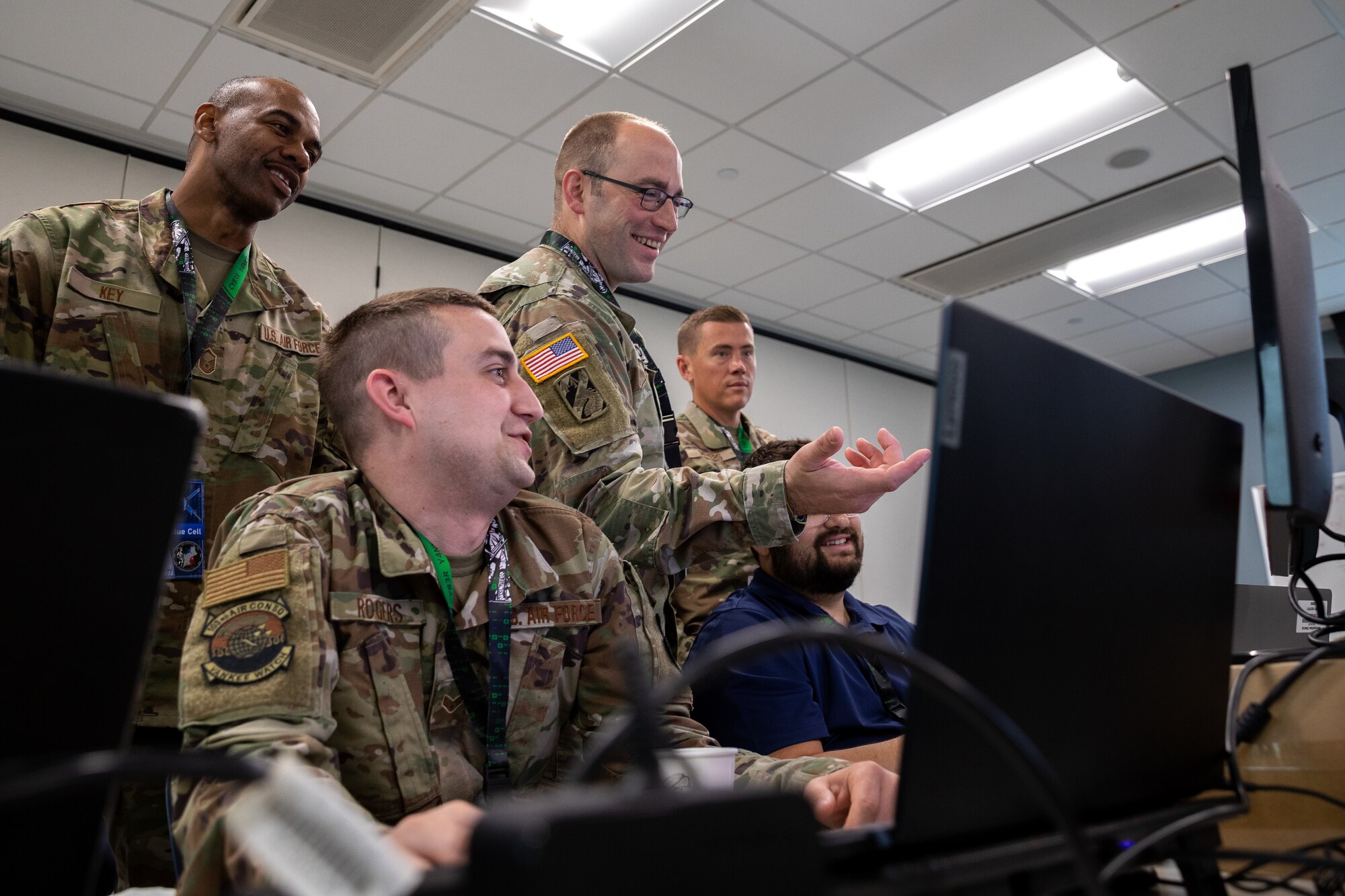 U.S. Army Staff Sgt. John Young, an information technology specialist assigned to Joint Forces Headquarters, Connecticut Army National Guard, points toward a computer monitor while communicating with U.S. Air Force airmen from 103rd Airlift Wing, Connecticut Air National Guard, at Camp Nett, Niantic, Connecticut, June 16, 2022. Soldiers and airmen from across Connecticut, and New England, worked hand in hand during Cyber Yankee to defend against a simulated cyber attack. (U.S. Army photo by Sgt. Matthew Lucibello)