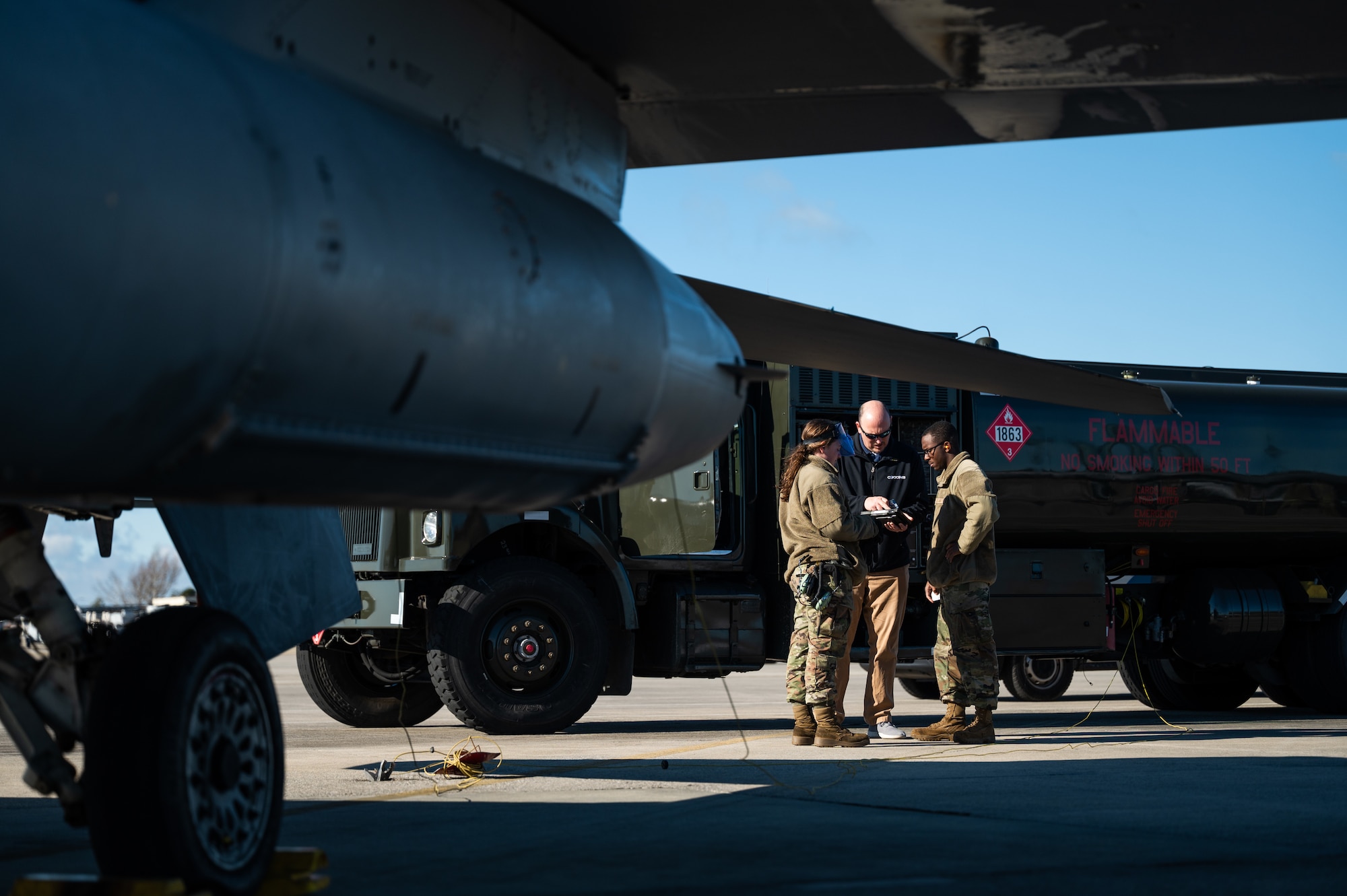 Three people look over a tablet and stand next to a fuel truck