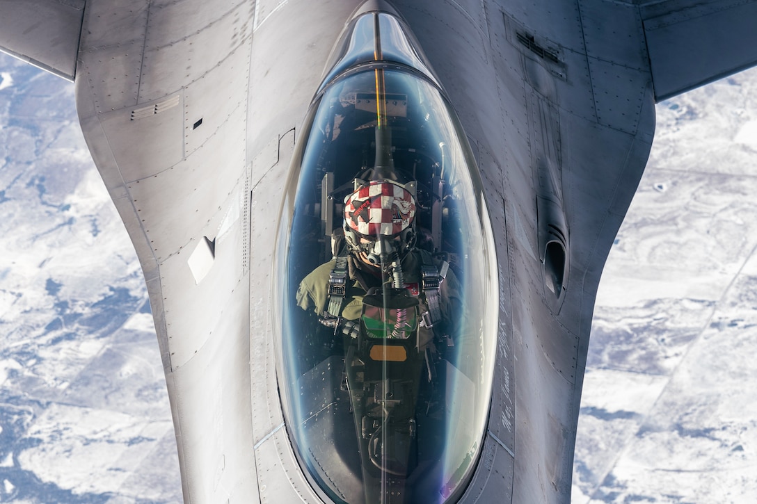 The pilot is seen in the cockpit as an F-16 Fighting Falcon hovers above clouds.