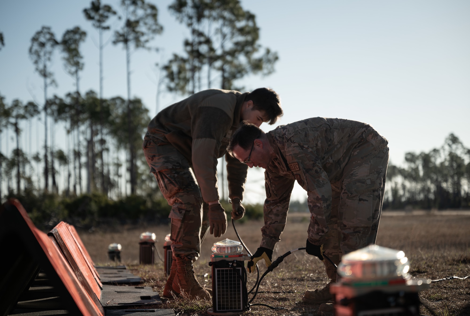 Two Airmen bend over an electrical system