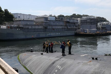 A Sailor assigned to the Ohio-class guided-missile submarine USS Michigan (SSGN 727) throws a messenger line to the pier upon arriving in Fleet Activities Yokosuka, July 2, 2023. Homeported in Naval Base Kitsap, Bangor, Washington, Michigan provides strike and special operation mission capabilities from a stealthy, clandestine platform.