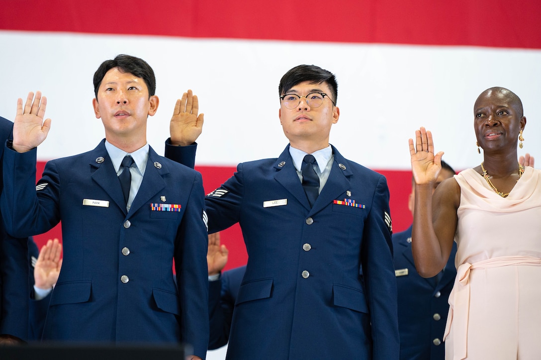 Three people stand before an American flag with their right hands raised.