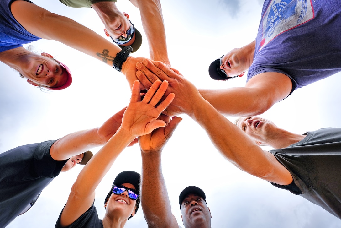 Soldiers are shown from below, participating in a huddle, during softball practice.