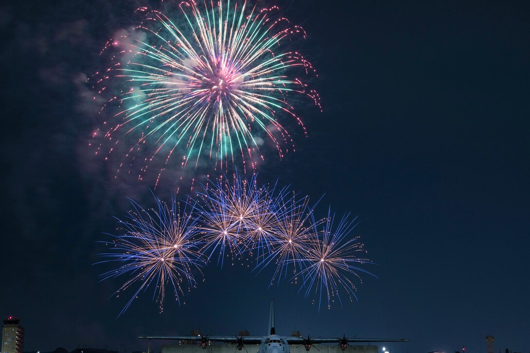 Fireworks explode behind a parked aircraft at night.