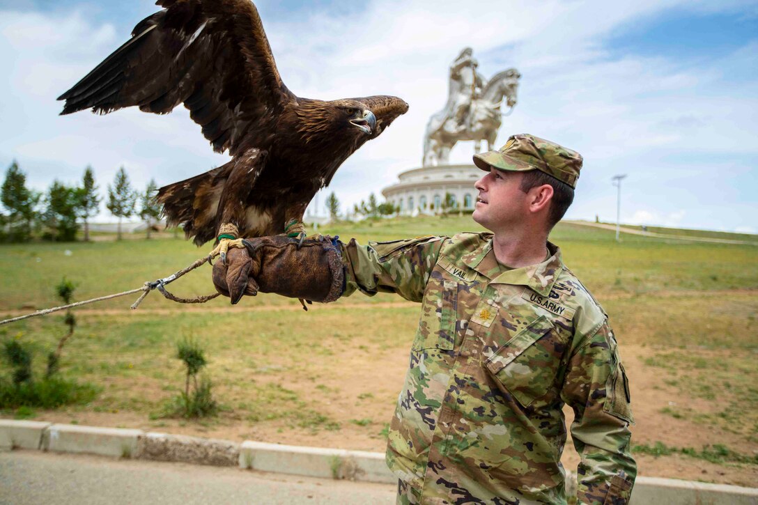 An eagle sits perched with its wings flapping on the outstretched arm of a guardsman.