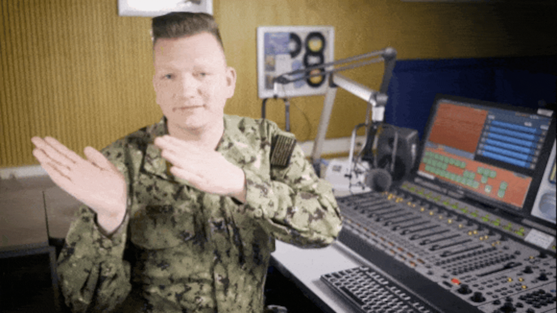A service member, with his hands up and palms facing each other, is moving his hands from one side to the middle of his body to demonstrate the hand signals and movements for communicating to a guest to bring their mouth back to the microphone.