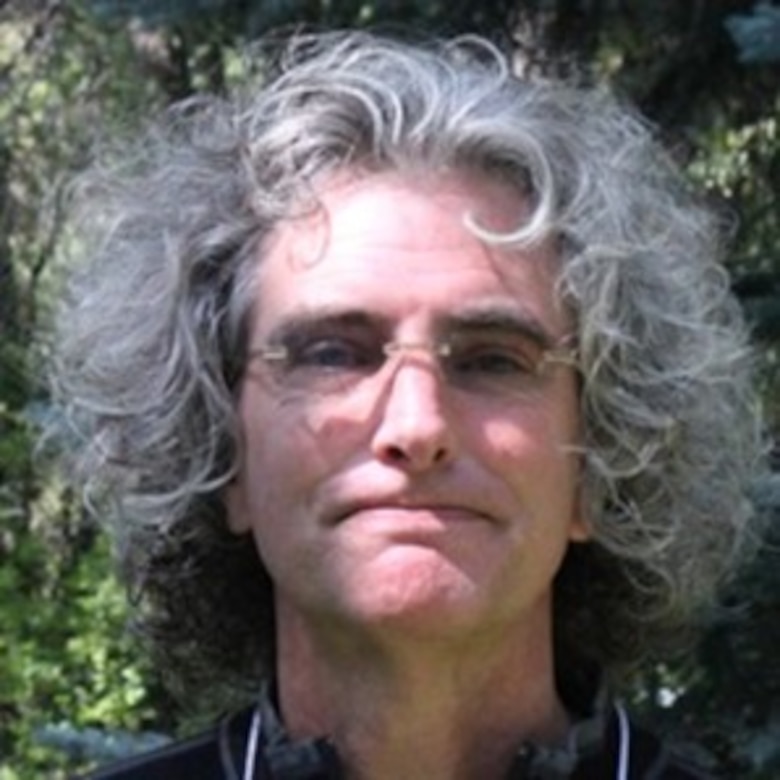 Photo of Caucasian man with long silver hair wearing glasses.