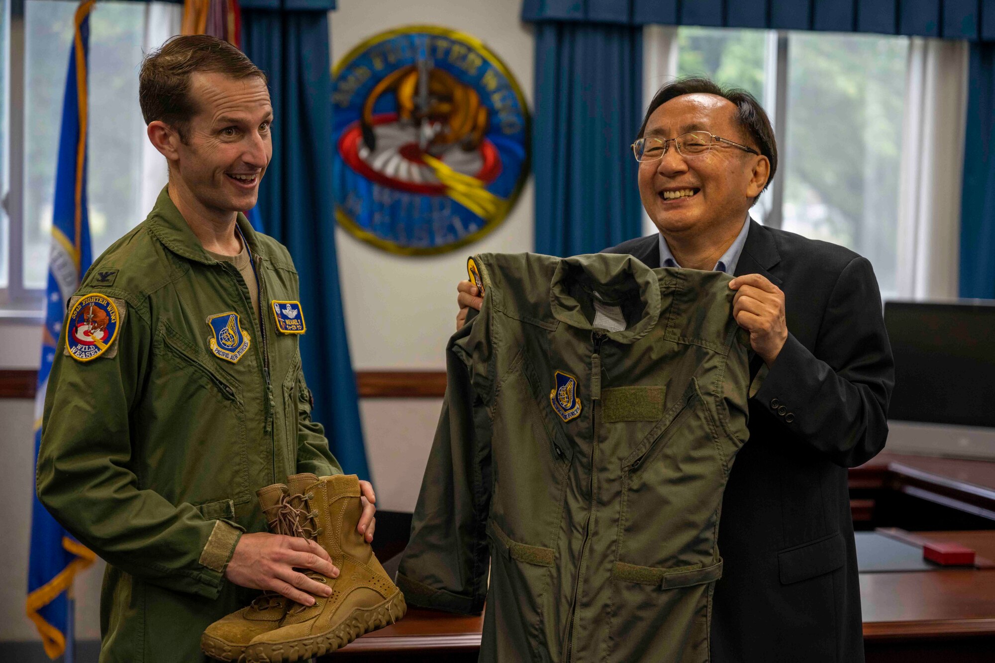 Two people pose with a flight suit while smiling.
