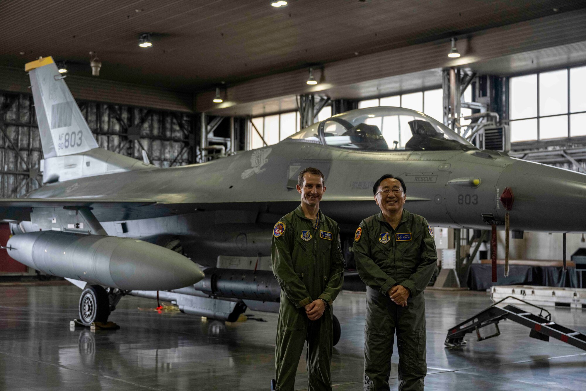 Two people pose in front of a fighter jet inside a hangar at Misawa Air Base.