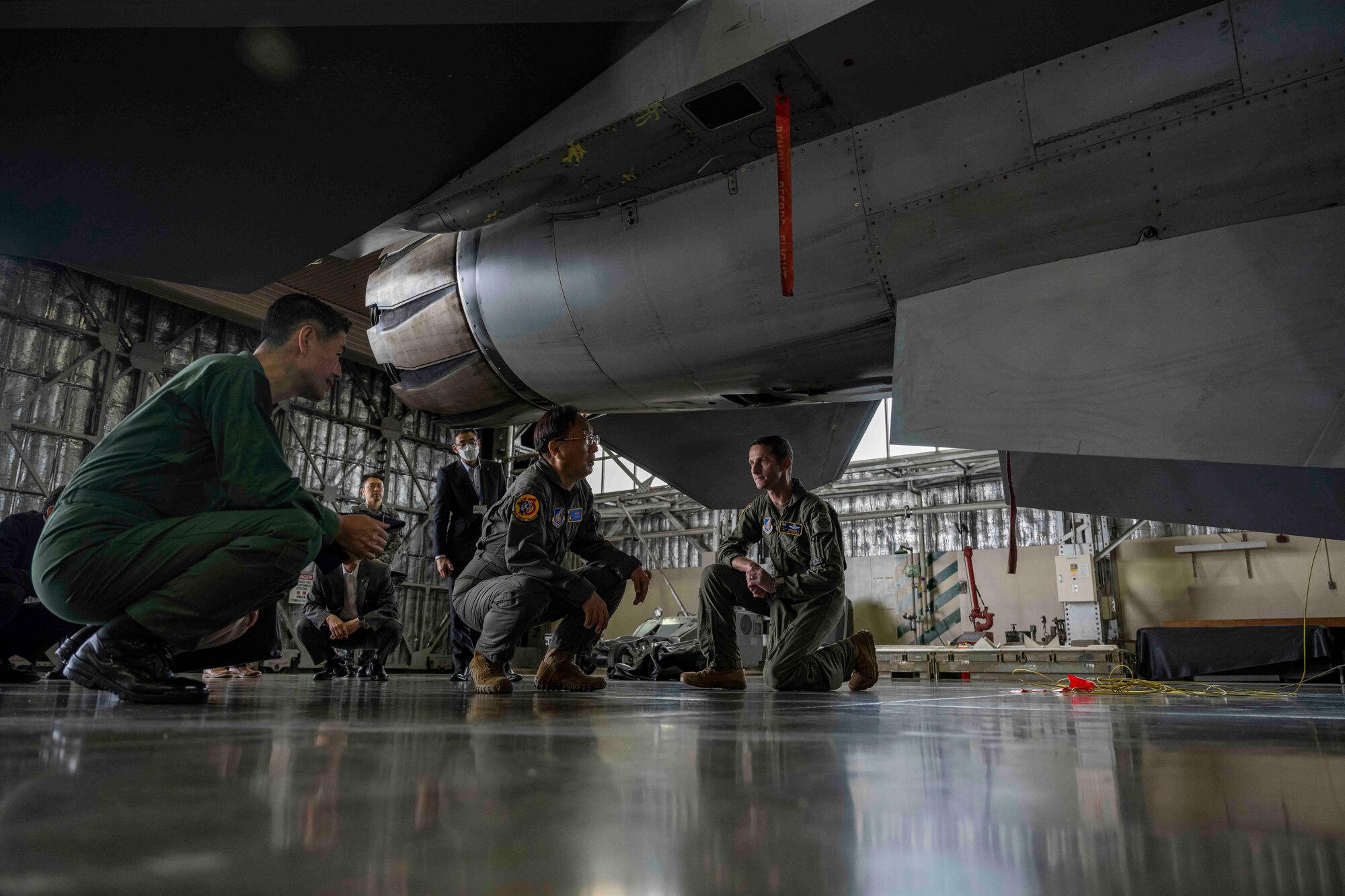 A group of people kneel as they look under a fighter jet in a hangar at Misawa Air Base.