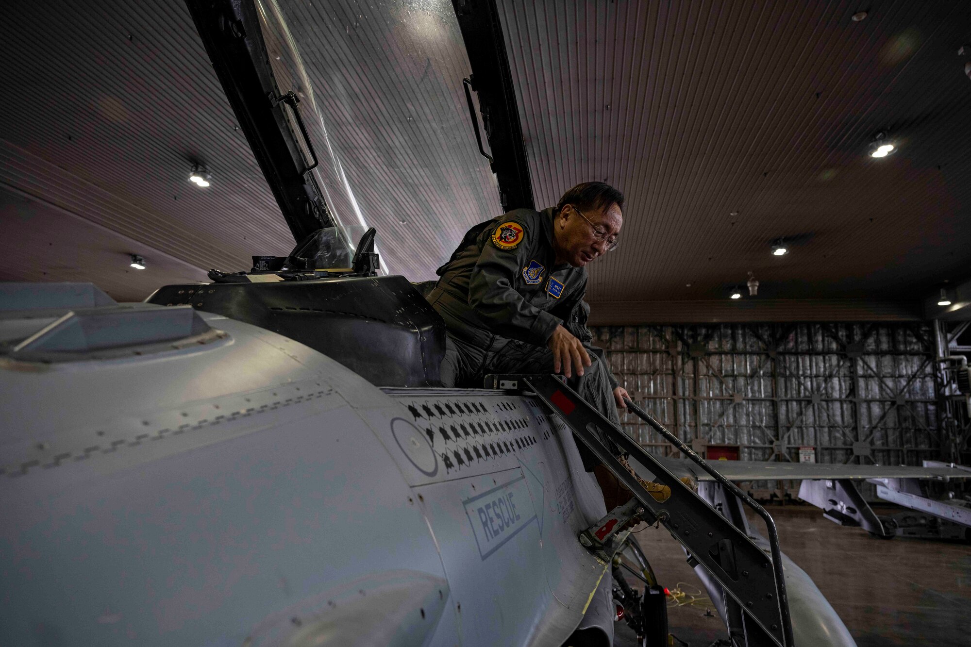 A man steps onto a ladder as he exits from the cockpit of the jet.