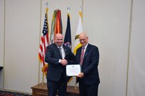 Department of the Army Criminal Investigation Division Deputy Directory, Robert Tracy, presents Guy Surian with a certificate of retirement for his 50 years of service to the U.S. Army.