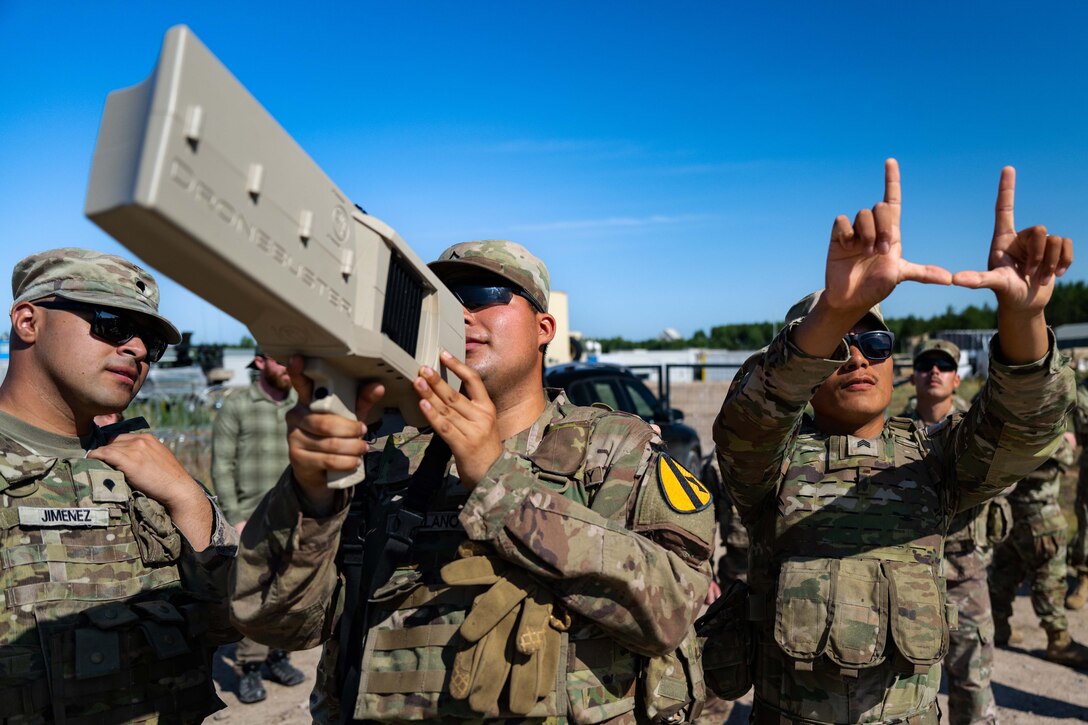 A soldier looks through a counter-unmanned aerial system while other soldiers look on.