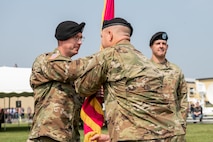 Photo of Sgt. Maj. Michael S. Riggs (left) receiving the Tobyhanna Army Depot (TYAD) flag from Col. James L. Crocker (right), signifying his assumption of responsibility as Tobyhanna Army Depot Sgt. Maj. In the background, outgoing Depot Commander Col. Daniel L. Horn observing the military ceremony.