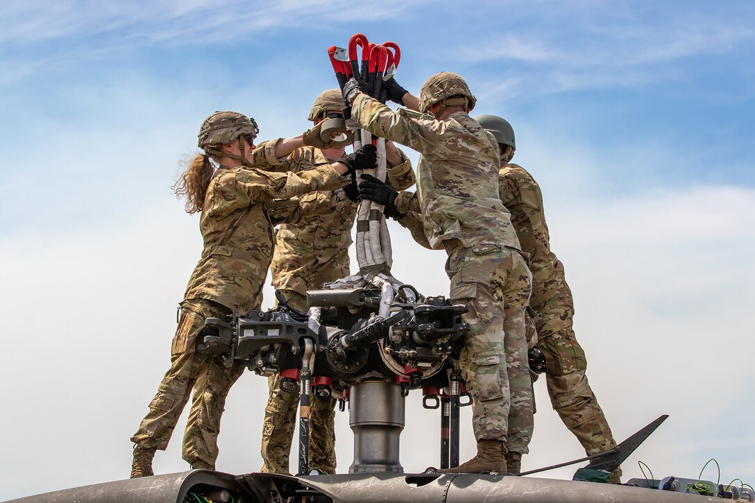 Soldiers stand in a circle atop a helicopter and hold up cords.