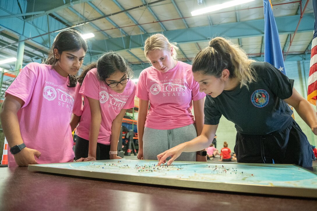 An airman points to locations on a map as girls watch.