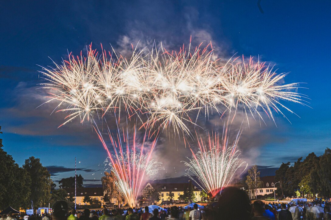 Fireworks explode in the sky as a crowd watches from below.