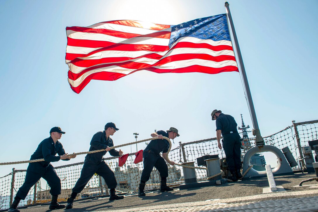 Sailors heave line aboard a ship as an American flag flies above.