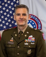 Male Army Soldier wearing AGSU poses in front of the United States and USAREC flags.